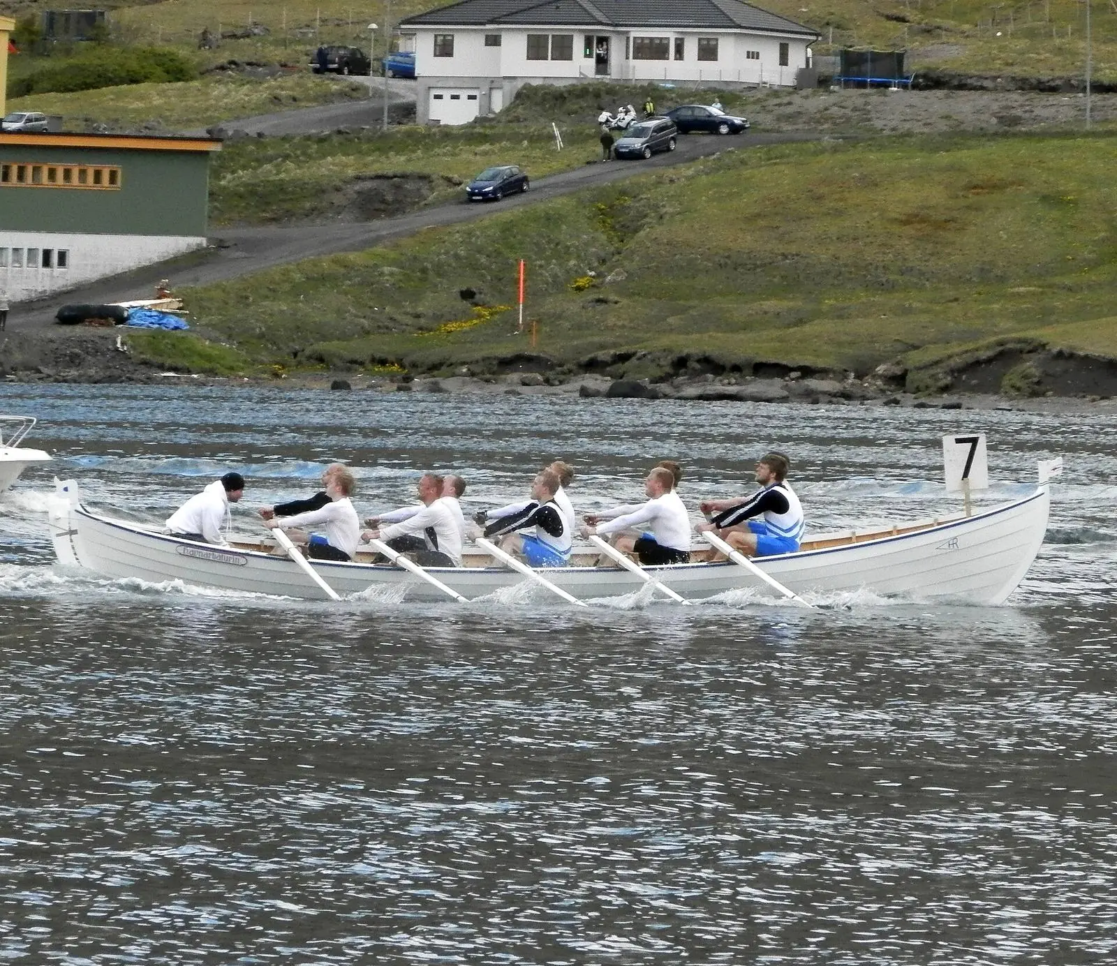 Un équipage d'aviron rame en cadence sur un bras de mer, le barreur à l'arrière.