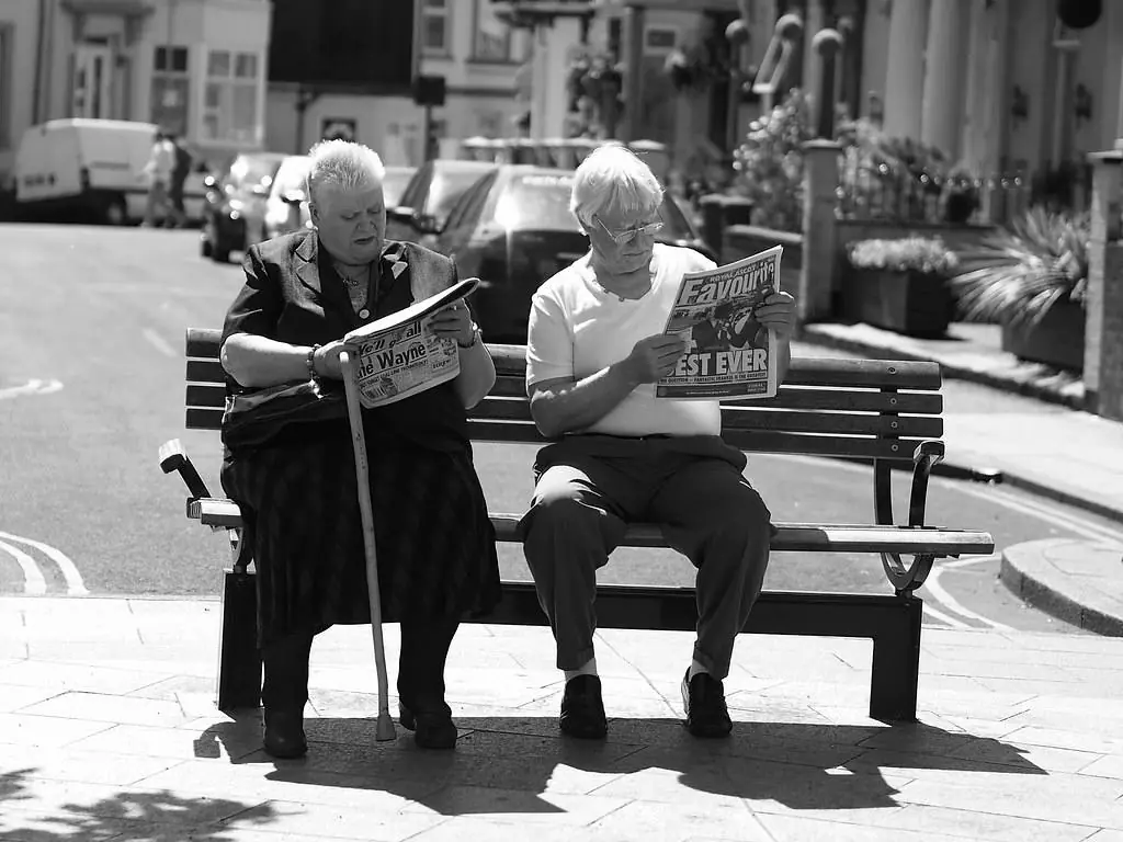 Deux hommes âgés lisent le journal sur un banc public.
