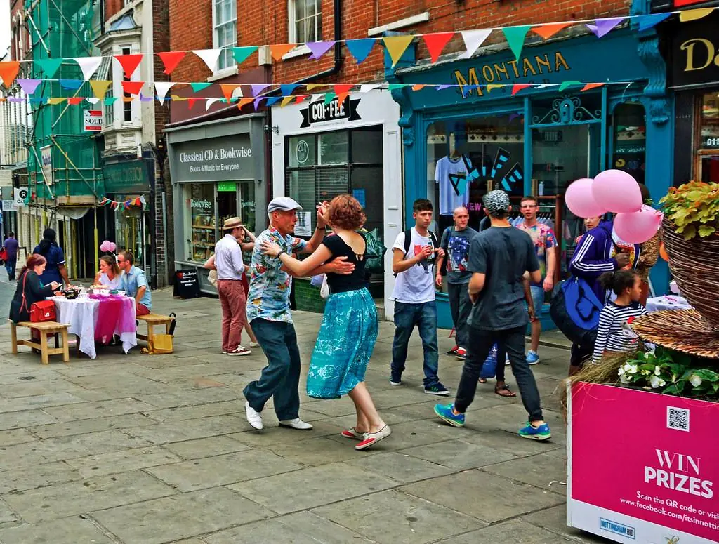 Un couple danse dans une rue piétonne pavoisée de fanions, un jour de fête.