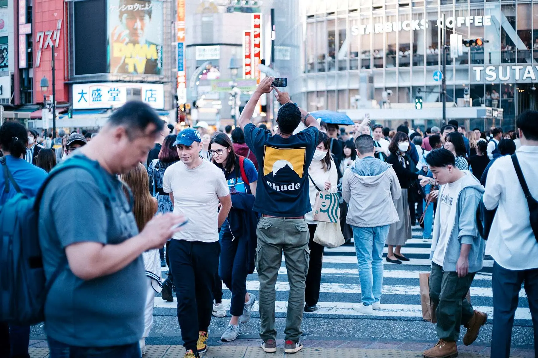 Une foule traverse un carrefour, un homme au premier plan regarde son téléphone.